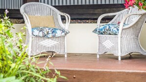 Two wicker chairs with cushions, a wooden deck, and a stone wall in the background. - Burleigh Coastal Escape 4BR Home (Burleigh Heads)