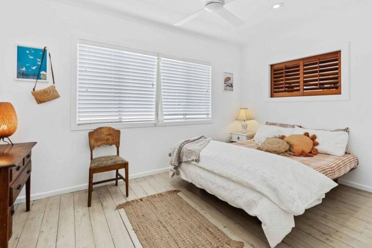 A bedroom with a bed, a chair, a desk, a lamp, and a window with blinds.