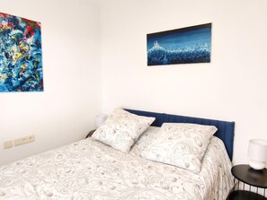 A bed with patterned bedding, a blue headboard, a nightstand with a lamp, and two wall-mounted paintings. - Casa Can Pep in Begur (Begur)