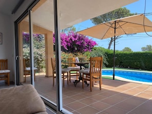 Un patio con mesa y sillas, una piscina y vistas a un jardín con flores moradas.