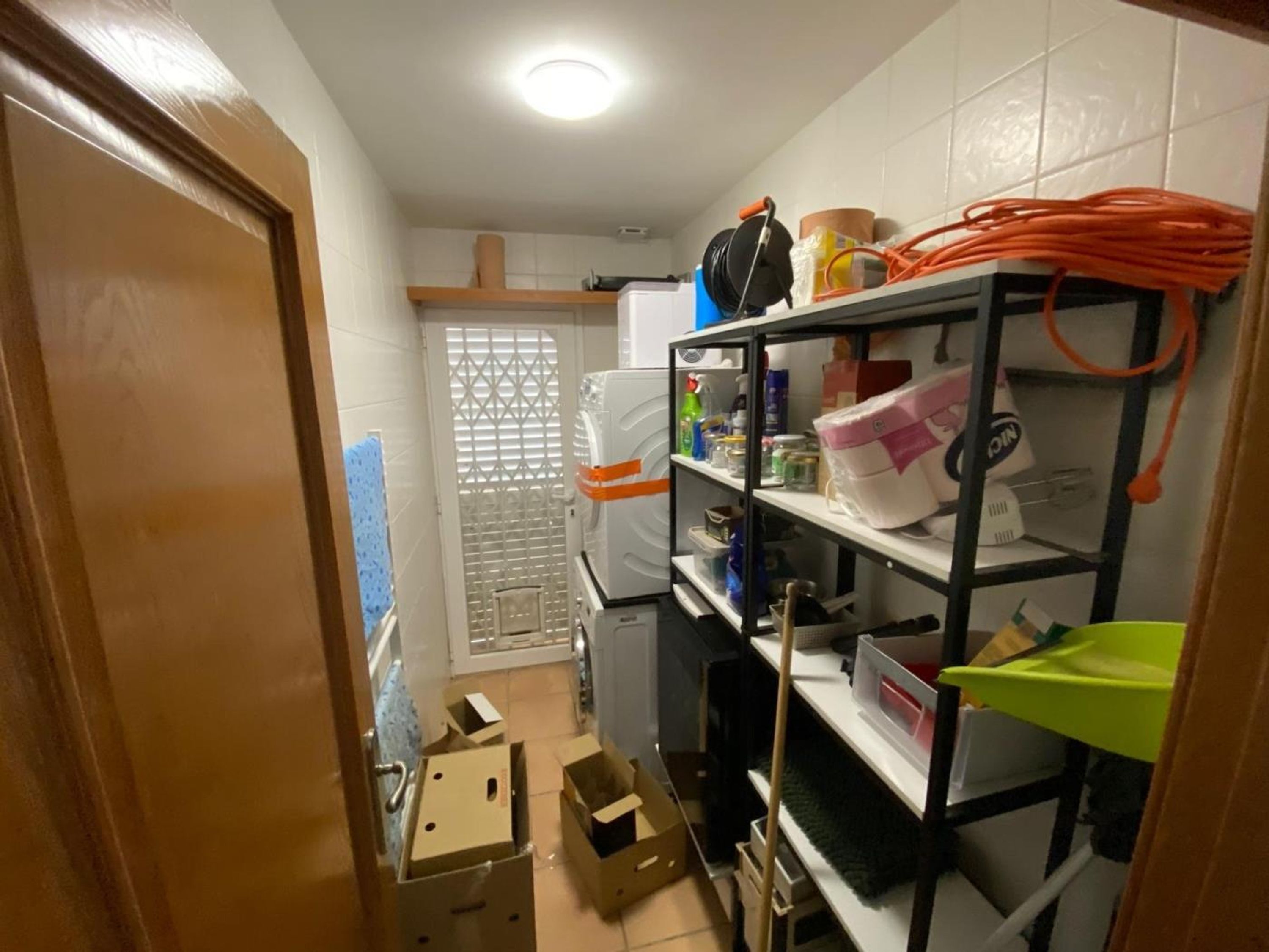Une petite pièce étroite comprenant un coin cuisine, une porte et une fenêtre avec des stores.