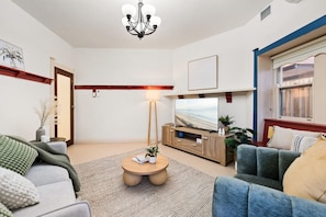 A living room with a TV, sofa, coffee table, and a chandelier. - Mosman 2BR Coastal Retreat | Balmoral & Harbour (Mosman)