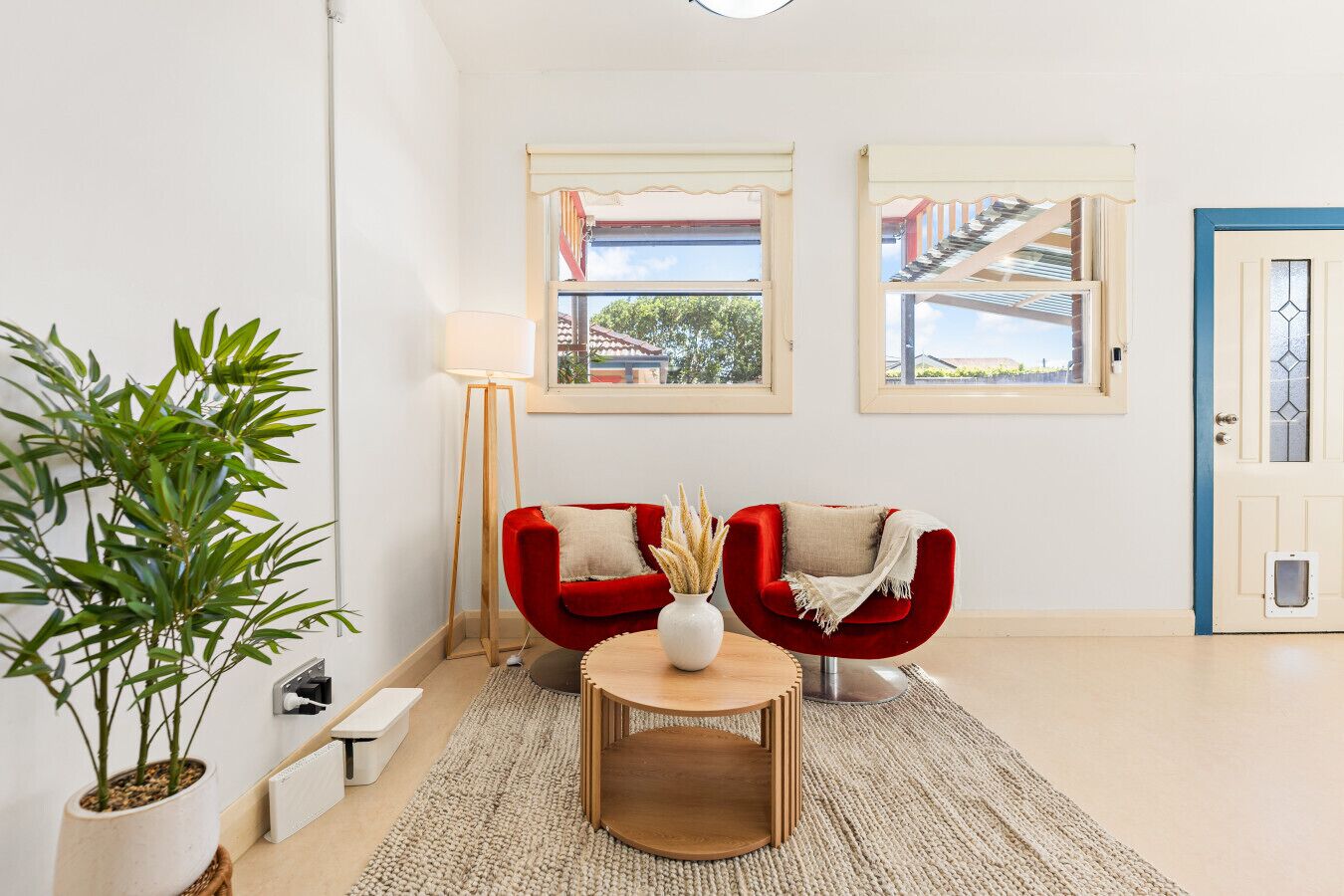 A room with two red chairs, a small round table, a floor lamp, and a potted plant.
