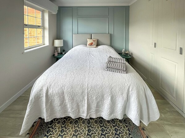 A bedroom with a large bed, a window, a nightstand, and a patterned rug.
