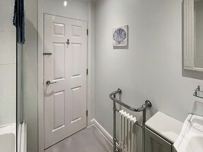 A bathroom with a white door, a glass shower enclosure, a white radiator, and a white sink.
