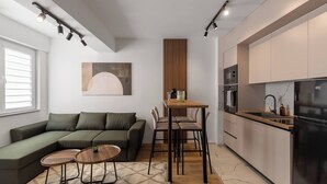 A modern living space with a sectional sofa, a dining table with chairs, a kitchen area with a refrigerator, and a large window.
