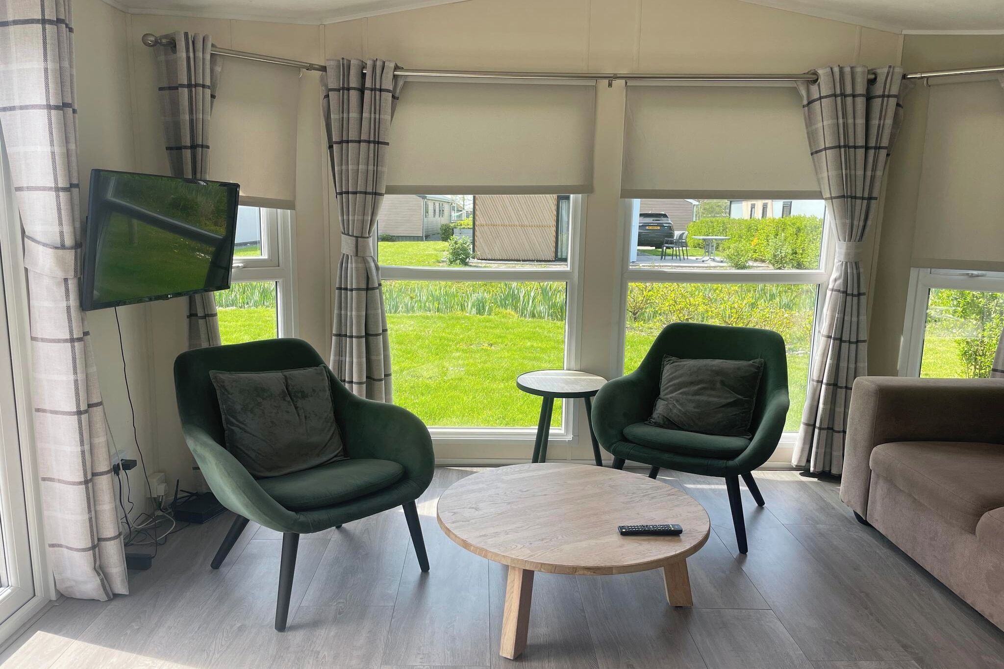 Een moderne woonkamer met een televisie, twee groene fauteuils, een ronde houten salontafel en een beige bank.