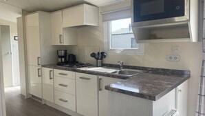 Una cocina moderna con armarios blancos, un microondas de acero inoxidable, un lavamanos y una ventana.