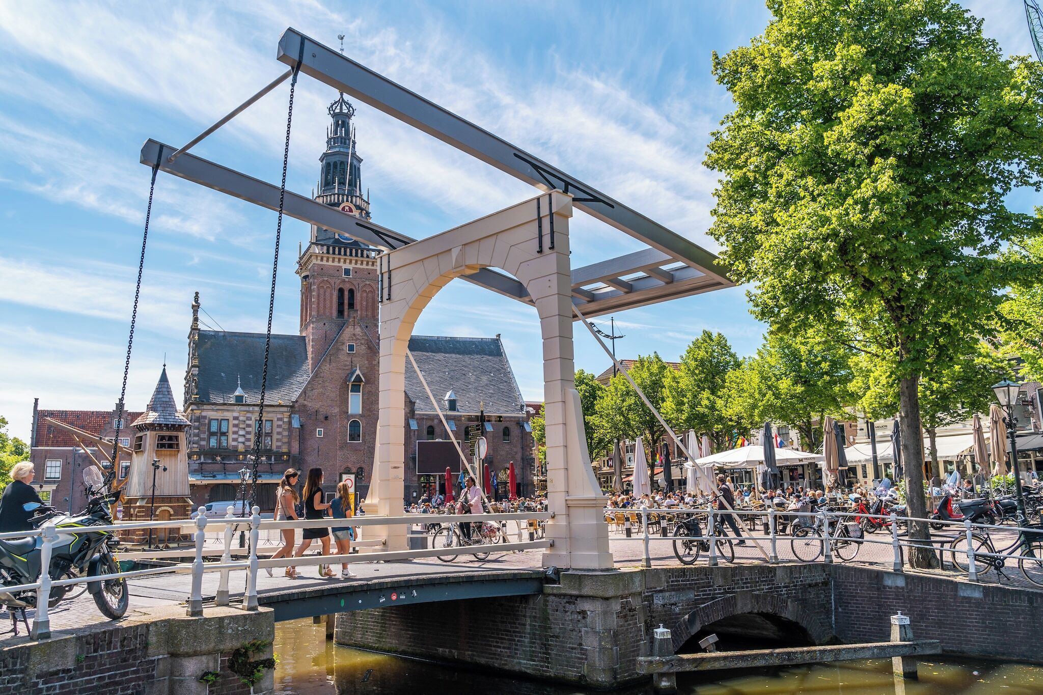 A historic bridge with a tower, a canal, and a bustling riverside walkway.