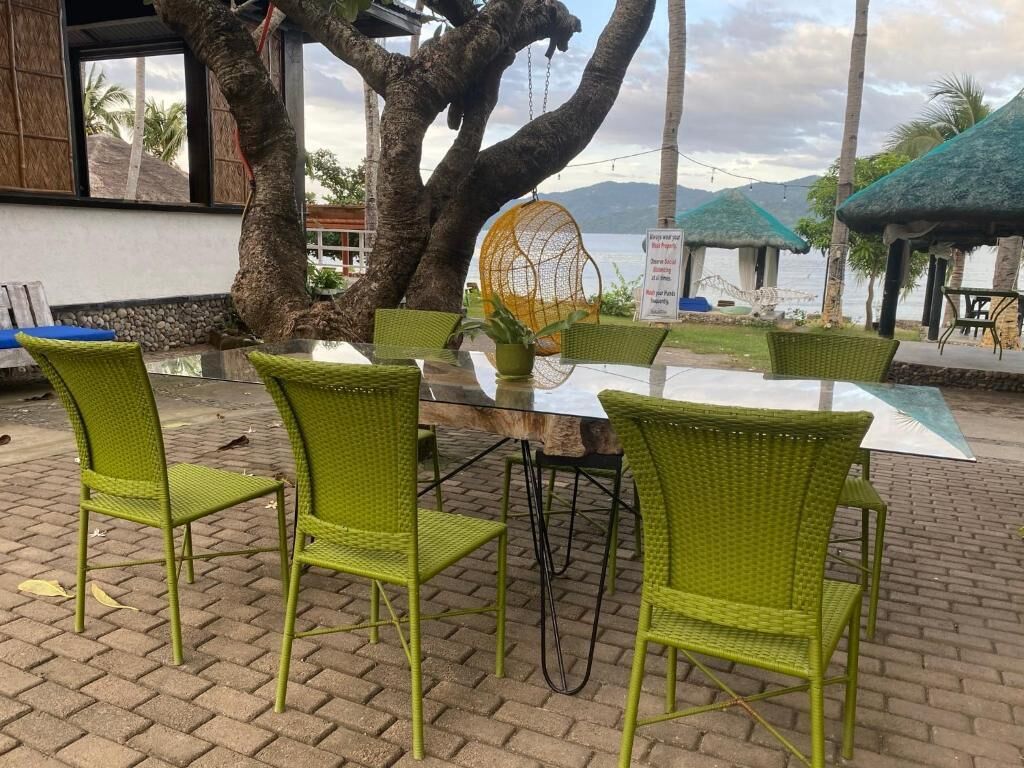 A table with chairs, a hanging chair, and a view of the sea.