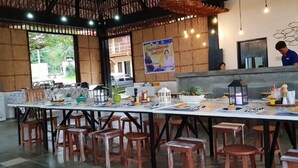 Un restaurant avec une longue table dressée pour le repas, des chaises en bois et un comptoir où une personne est assise.