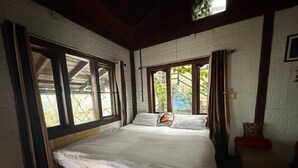 Een enkel bed met een houten frame, wit beddengoed en uitzicht op groen door grote ramen.