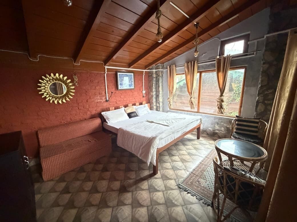 Un dormitorio con cama, sofá, una mesita y una ventana con cortinas.
