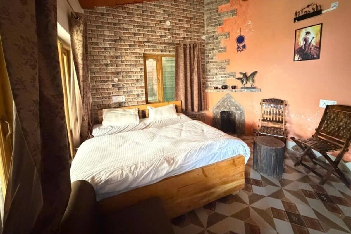 A room with a brick wall, a bed, a chair, and a small table.