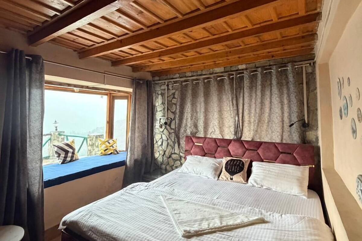 A wooden ceiling, a bed with a headboard, a window with curtains, and a wall with a decorative plate.