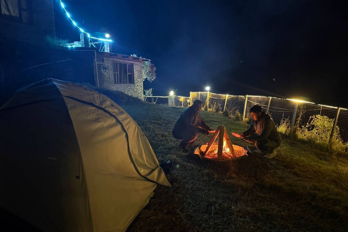 A tent and a campfire with two people around it.