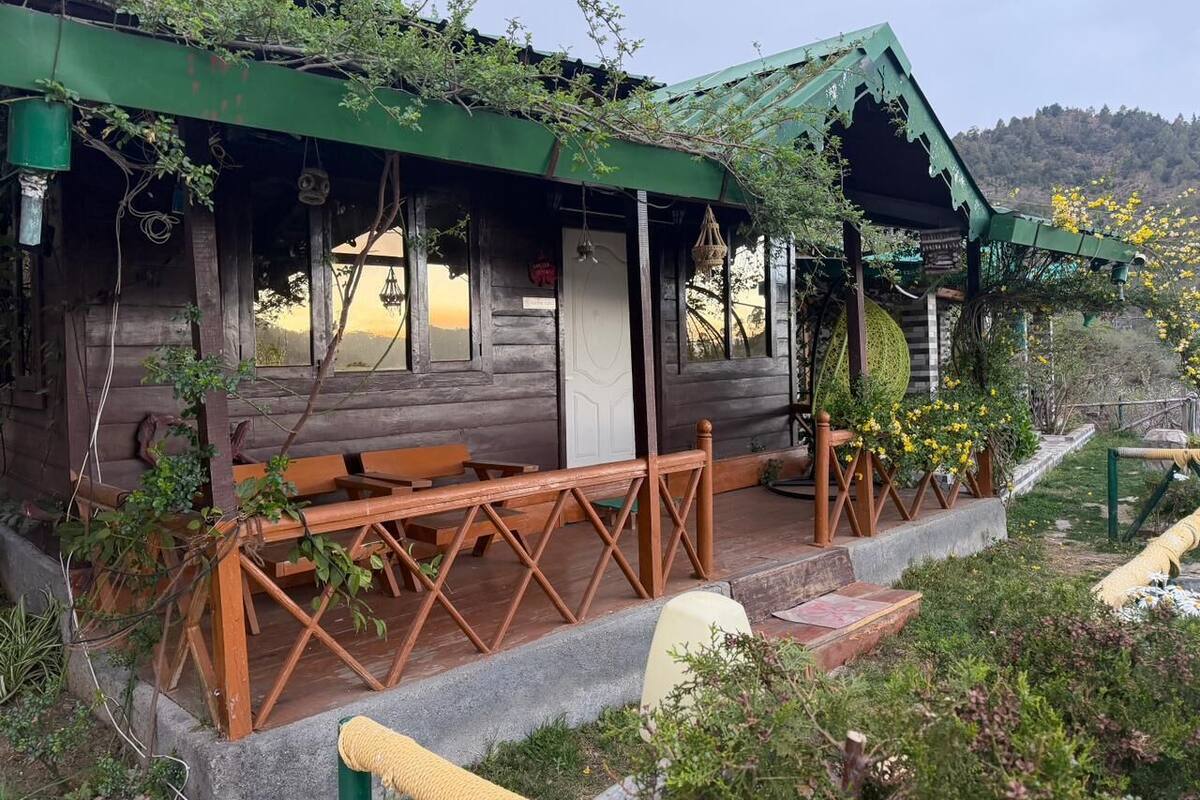 A rustic wooden cabin with a porch, benches, and a small garden area.