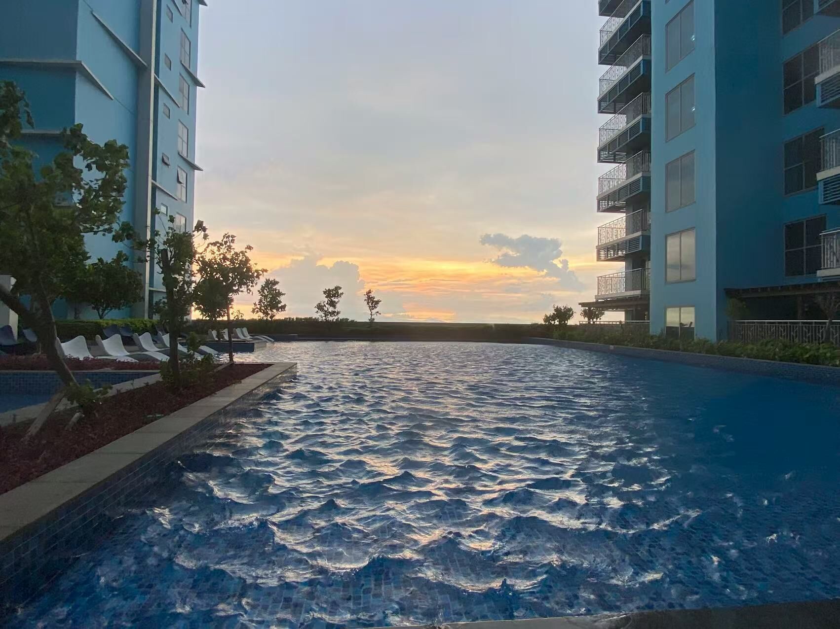 A swimming pool with a sunset view, surrounded by modern buildings with balconies.