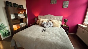 Un dormitorio con una cama grande, una mesita de noche con lámpara, una estantería de madera y una ventana con vistas.