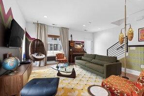 Ein modernes Wohnzimmer mit einer Couch, einem Hängesessel, einem Glastisch, einem Globus und einem Klavier.