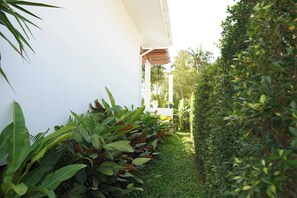 A narrow pathway flanked by lush greenery and a white building. - O3 Green 2b Garden Pool Villa and Unique Furniture (Tambon Ko Pha-ngan)