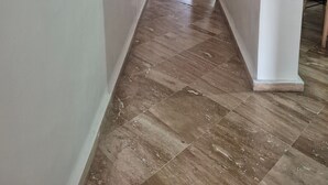 Een gang met een marmeren vloer, witte muren en een deur die naar een andere kamer leidt.