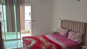 Een slaapkamer met een bed, nachtkastje, kapstok en raam voorzien van gordijnen, plus een airconditioner.