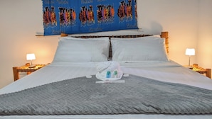 Une chambre d’hôtel avec un grand lit, du linge de lit blanc, une tapisserie bleue ornée de motifs, deux lampes de chevet et un plaid gris.