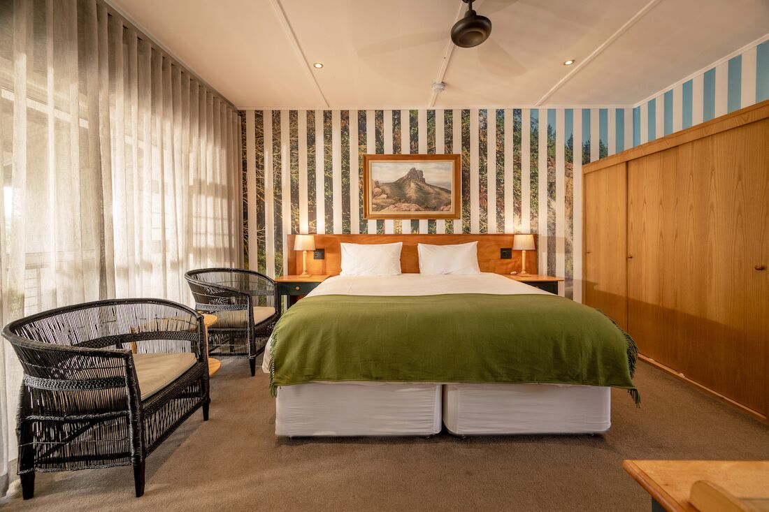 A bedroom with a large bed, two bedside tables, a chair, and a wooden wardrobe.