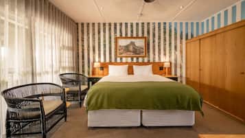 A bedroom with a large bed, two bedside tables, a chair, and a wooden wardrobe.