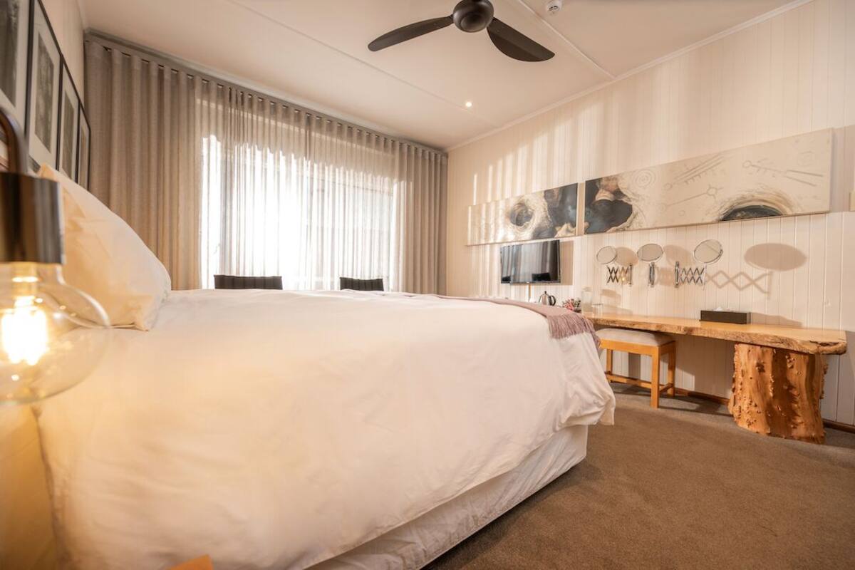 A bedroom with a large bed, a ceiling fan, a wooden bench, and a wall-mounted TV.