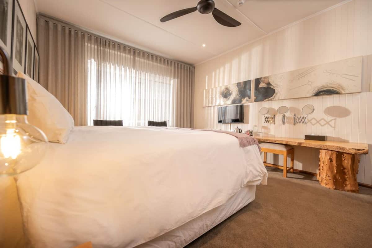 A bedroom with a large bed, a ceiling fan, a wooden bench, and a wall-mounted TV.