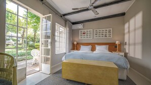 Une chambre à coucher comprenant un lit, des tables de chevet, un ventilateur de plafond, une fenêtre et une porte donnant sur un balcon.