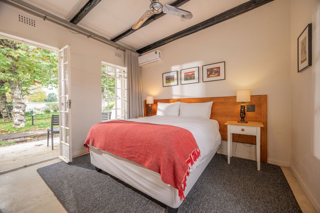A bedroom with a bed, a nightstand, a ceiling fan, and a window with a view of greenery.