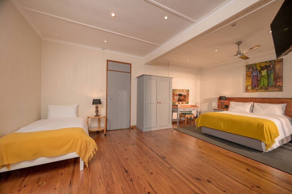 A bedroom with two beds, a desk, a wardrobe, and a ceiling fan.