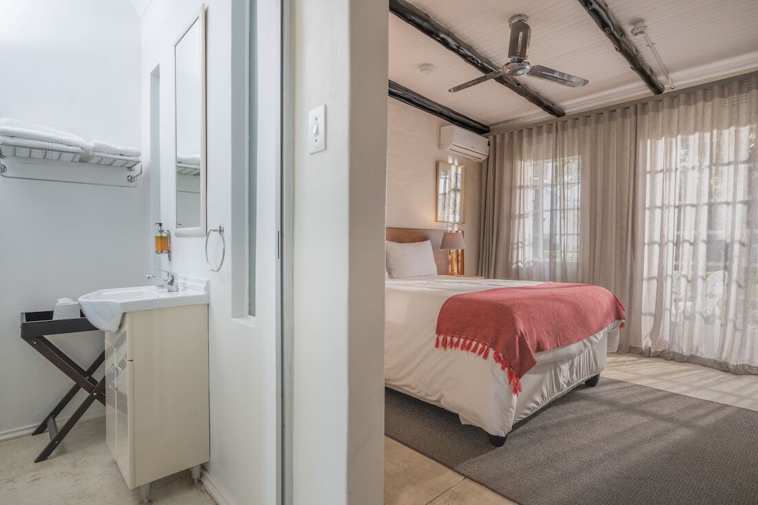 Ein Hotelzimmer mit einem weißen Waschbecken, einem Spiegel und einem Bett mit roter Decke.