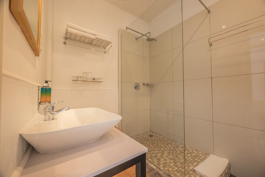 Un baño con lavamanos blanco, cabina de ducha de vidrio y piso de baldosas.