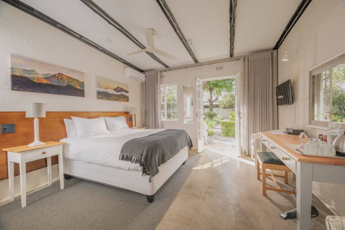 A bedroom with a bed, bedside table, desk, chair, and a view of the outdoors.