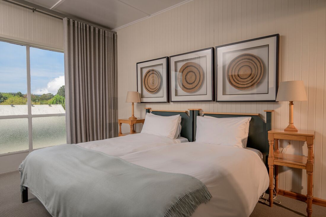 Une chambre d’hôtel avec un grand lit, deux tables de chevet, une fenêtre avec des rideaux et trois œuvres d’art encadrées accrochées au mur.