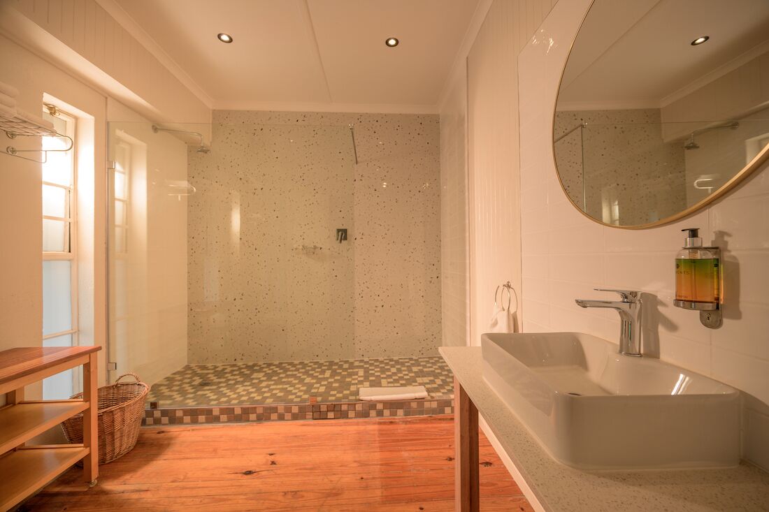 Un baño con ducha, lavamanos, espejo y suelo de madera.