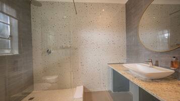 A modern bathroom with a glass-enclosed shower, a freestanding sink, and a large mirror.