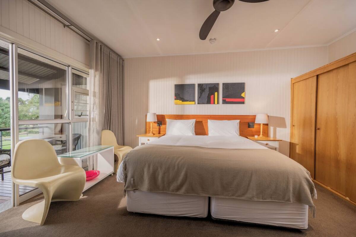 A hotel room with a bed, a desk, a chair, a window, and a door.