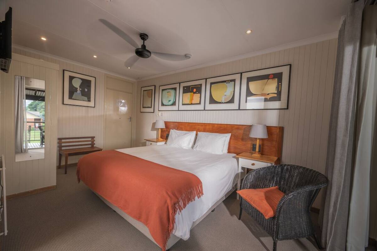 A hotel room with a large bed, a ceiling fan, a chair, and artwork on the wall.