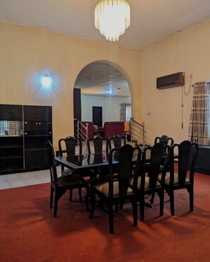 A dining area with a table and chairs, an arched doorway, a staircase, and an air conditioning unit.