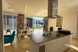 A modern kitchen with a central island, a dining area with a glass wall, and a view of the outdoors.