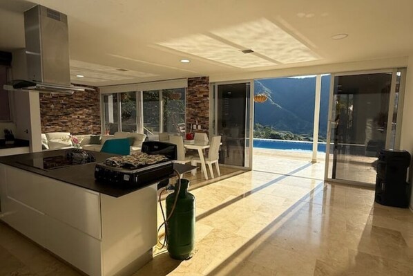 A modern kitchen with a central island, a dining area with a view, and a large sliding glass door leading to a balcony.