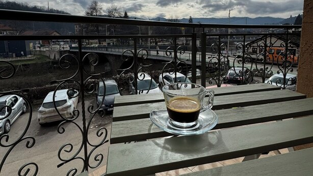 Un balcón con una mesa de vidrio que sostiene una taza de café, con vistas a un estacionamiento y un puente.