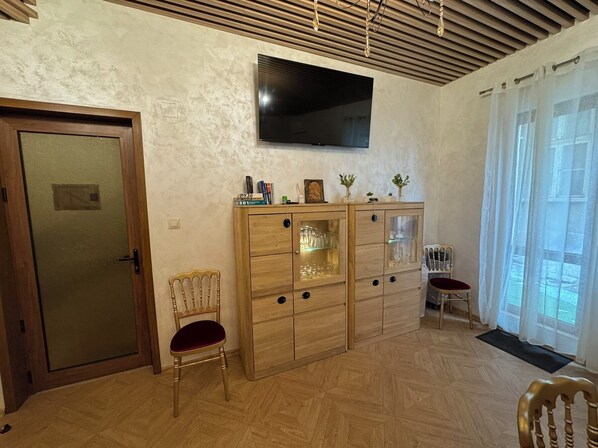 Une pièce avec un meuble en bois, un téléviseur fixé au mur, une chaise et une porte.