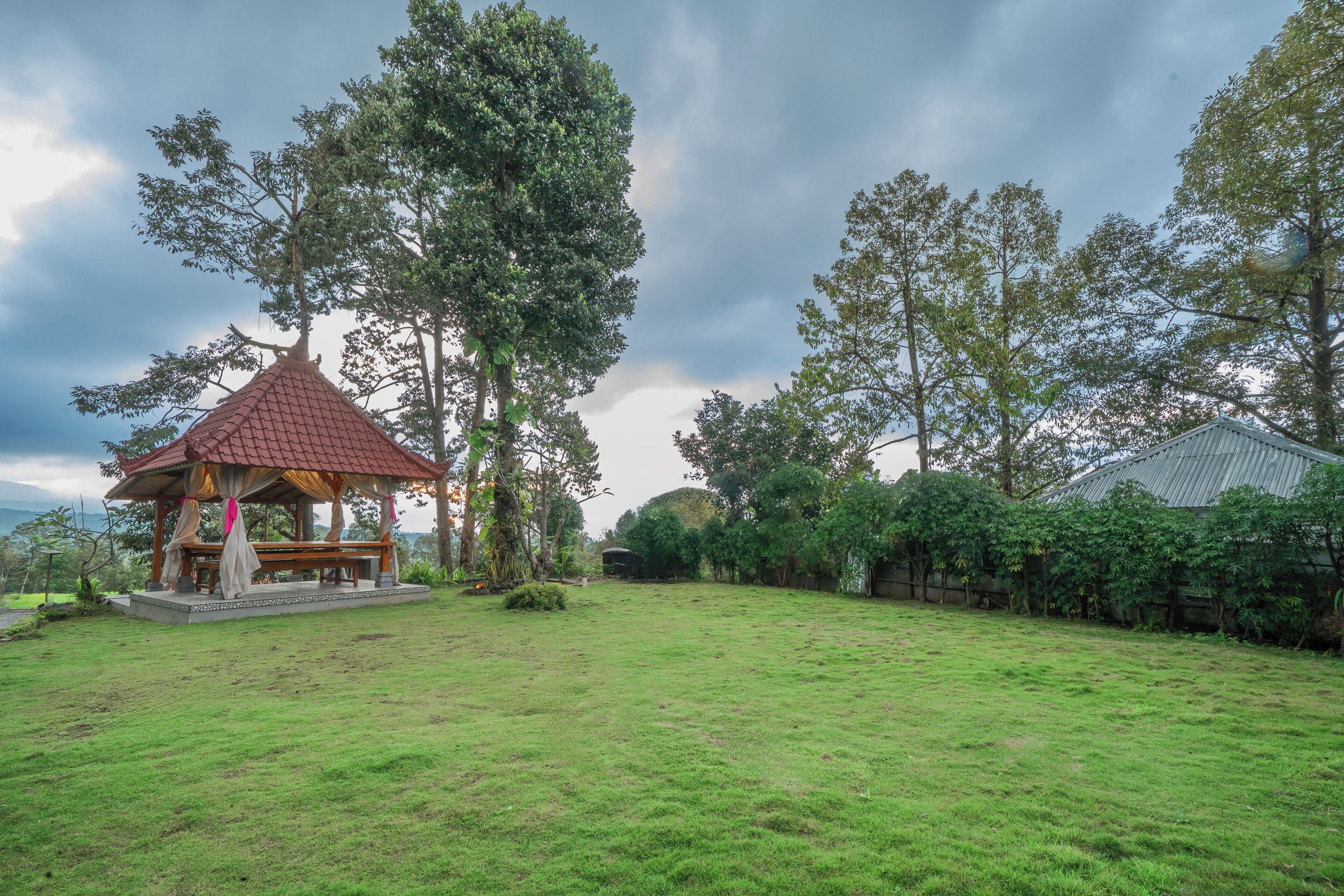 A gazebo with a red roof and a bench, surrounded by a grassy yard and trees.
