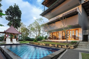 Un hotel moderno con piscina, mobiliario exterior y zona cubierta.